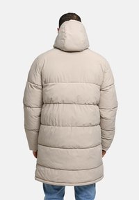 Beige puffer coat, knee-length, quilted design with a large hood, visible stitching, resting on a person seen from the back.