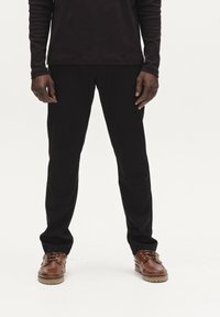 Svarta skräddarsydda byxor i ett glatt material, tillsammans med bruna läderskor med kraftig sula och snörning.