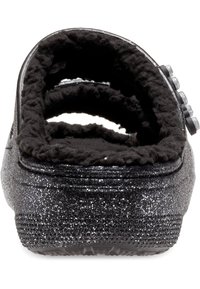 Scarpa slip-on nera con glitter, caratterizzata da una morbida fodera interna in pelliccia nera e suola testurizzata. Tre bottoni decorativi sul lato.