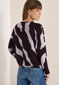 Sweter w kolorze burgundowym i szarym w wzory, o luźnym kroju, szerokich rękawach i ściągaczu. Noszony z niebieskimi dżinsami, prezentując swobodny strój.