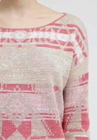 Pletený svetr s geometrickým vzorem v růžových a krémových odstínech. Výstřih ve tvaru lodi, volný střih a texturovaná tkanina.