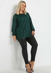 Grön spetsblus med långa ärmar och scallopkant, i kombination med svarta imitation läder leggings och svarta sandaler med remmar. Slät textur och figurnära design.