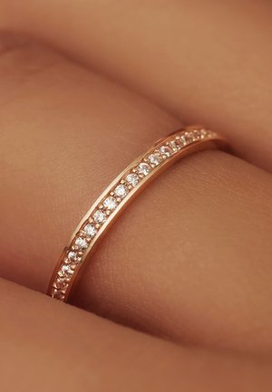 Bague en or rose avec un anneau fin, ornée de petites pierres transparentes le long du bord supérieur, surface lisse et finition polie.