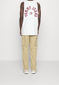 Vit ärmlös skjorta med "TOMMY JEANS" tryckt i röda bågar på baksidan, ihop med ljusbeiga cargobyxor och krämfärgade sneakers.