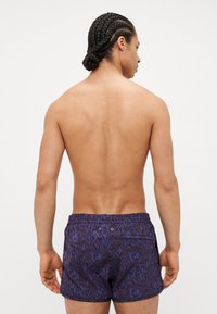 Maillots de bain de couleur bleu foncé avec un motif abstrait texturé. Comprend une taille élastique et une poche arrière avec deux œillets en métal.