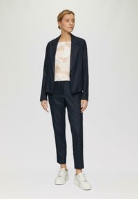 Blazer à carreaux navy, pantalon assorti et un haut à motifs légers. Stylé avec des baskets à plateforme blanches. Texture plate, coupe ajustée.
