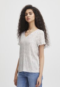 Maglietta a V in tessuto leggero con righe verticali rosa, blu e viola su base bianca. Maniche corte e vestibilità rilassata.