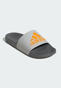 Gray slide sandal with an orange Adidas logo on a textured strap. Rubber sole, flat design, open toe, and contrasting colors.