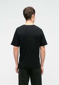 Melnas kokvilnas t-krekls ar īsām piedurknēm un apaļu kakla izgriezumu, kam ir vienkrāsains raksts bez modeļiem vai akcentiem. Minimālistisks dizains.