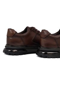 Bruine leren schoenen met een gestructureerd oppervlak, ronde neus en zwarte rubberen zool. Ze hebben een vetersluiting en geperforeerde details.