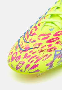 Crampons de soccer jaunes vifs avec un motif imprimé animal rose et violet, présentant une surface texturée et un système de laçage proéminent. Studs transparents.