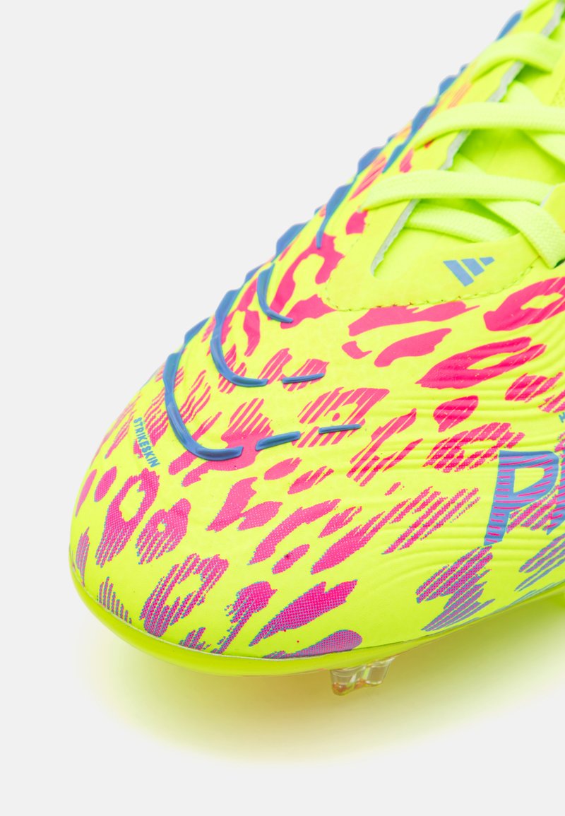 Bota de fútbol amarilla brillante con un patrón de estampado animal en rosa y púrpura, con una superficie texturizada y un sistema de cordones prominente. Tapones transparentes.