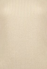 Cremfarbener Strickpullover mit geripptem Muster und nahtlosem Design, das ein glattes, einheitliches Erscheinungsbild betont.