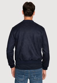 Chaqueta bomber de ante azul marino con puños y dobladillo acanalados, que presenta un diseño sencillo y un acabado texturizado. Adecuada para uso casual.