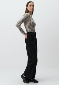Top lungo a maniche, aderente, in grigio e beige con motivo tie-dye, abbinato a pantaloni a gamba larga neri a vita alta e mocassini neri senza lacci.