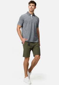 Polo gris avec un col blanc et des accents rayés, associé à un short vert olive et des baskets blanches. Textile lisse, coupe décontractée.