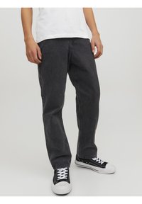 Svarta denimjeans med en avslappnad passform, med en klassisk femfickdesign och synlig sömnad, ihop med svarta och vita sneakers.