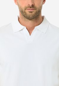 Weißes Poloshirt mit klassischem Kragen und einem subtil strukturierten Stoff. Das Design umfasst eine Drei-Knopf-Leiste und einen sauberen, minimalistischen Look.