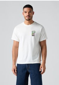 Hvit bomulls T-skjorte med et kaktusmotiv i grønn og lilla, med en svart Levi's-logo på brystet. Kort erm og rund hals.