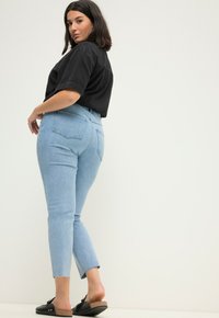 Vaqueros de tiro alto azul claro con un dobladillo sin terminar, combinados con una camiseta negra corta y zapatos de deslizamiento negros. Con bolsillos visibles y un ajuste relajado.