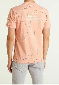 Kurzarm-T-Shirt in Pfirsichfarbe mit einem Graufleckmuster und Druck auf der Rückseite. Weicher Baumwollstoff mit einem lockeren Schnitt.