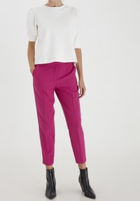 Valkoinen puuvillapaita puffihihalla yhdistettynä kirkkaanpunaiseen räätälöityyn housupariin. Mustat nilkkabootsit täydentävät asu.