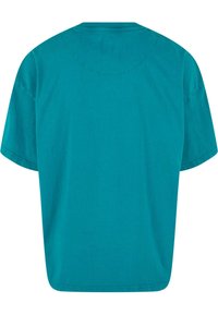 Tirkīza krāsas kokvilnas T-krekls ar brīvu piegriezumu, īsām piedurknēm un noapaļotu kakla izgriezumu. Aizmugures skats parāda gludu tekstūru un kārtīgu šuvumu.