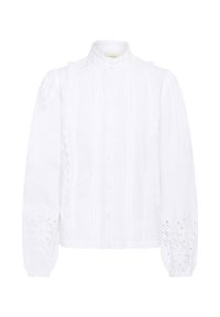 Blouse blanche en tissu texturé, avec un col haut, un devant plissé et des accents en œillets délicats sur les manches.