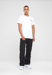 White cotton t-shirt with short sleeves and a small black graphic on the chest, paired with black cargo pants featuring zip pockets.