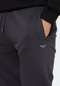 Dunkelgraue Sweatpants aus weichem Material mit einer Seitentasche und einem kleinen gestickten Logo auf dem linken Oberschenkel.