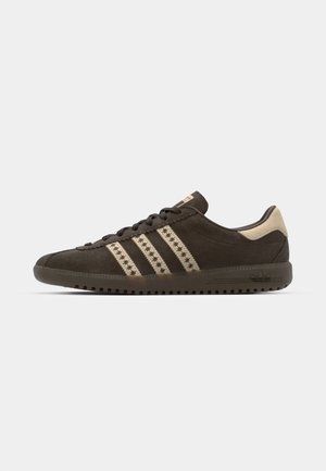 Sneaker in suede marrone con accenti beige, caratterizzato da tre strisce beige e una suola in gomma testurizzata. I lacci sono di un marrone scuro.