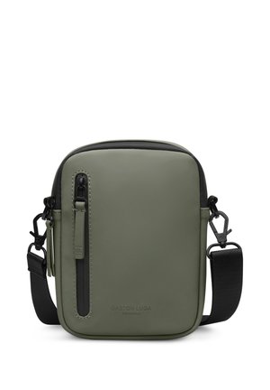 Compacte crossbodytas in olijfgroen met zwarte verstelbare riem, verticale voorzak met ritssluiting en een gladde matte afwerking.