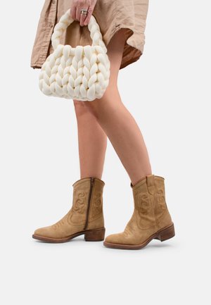 Bottines en cuir suédé marron avec un motif brodé et une fermeture éclair sur le côté, accompagnées d'un sac à main tissé blanc. La tenue comprend une robe beige.