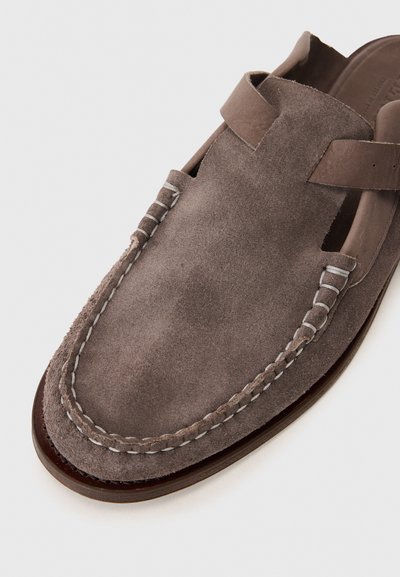 Scarpa slip-on in suede grigio con fianchi a taglio, cuciture bianche lungo i bordi e una soletta liscia in pelle marrone. Suola piatta.
