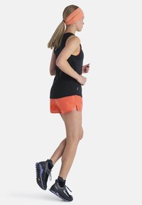 Top negro de tirantes combinado con pantalones cortos naranjas, zapatillas deportivas con detalles en negro y púrpura, y una diadema naranja a juego.