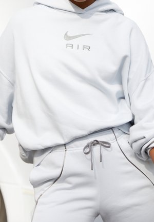 Personne portant un sweat à capuche blanc Nike Air et un pantalon de survêtement blanc assorti avec un cordon gris et des accents de couture.
