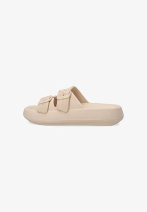 Beige slip-on sandals with two adjustable buckles, textured material, and a thick, ridged sole for enhanced grip and comfort.