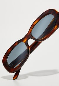 Ochelari de soare supradimensionați din scoică cu lentile gri, textură netedă, formă rotundă și branding subtil pe ramă.