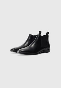 Botas Chelsea negras de cuero con una textura suave, paneles laterales elásticos y asas para facilitar el calzado. Diseño de punta redonda y tacón bajo.