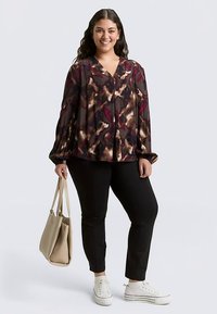 Long-sleeve blouse with a multicolored abstract pattern in dark tones, featuring a V-neck and pleated design, paired with black pants and sneakers.