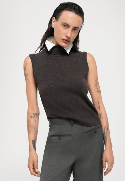 Brown sleeveless turtleneck sweater with a high neck and white collar, paired with tailored gray trousers featuring side pockets and button details.