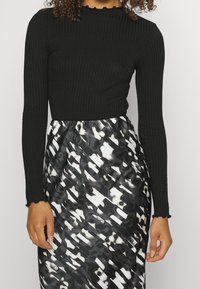 Haut long noir à rayures avec un col festonné, associé à une jupe fluide noire et blanche ornée de formes abstraites.