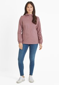 Lightweight, hooded jacket in light mauve with zip closure. Features elastic cuffs and smooth texture, paired with slim-fit blue jeans and white sneakers.