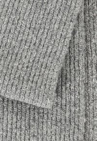 Szary, dziany materiał o ryflowanej fakturze; charakteryzuje się luźnymi ściegami i miękkim, puszystym wyglądem. Widoczne są warstwy materiału.