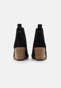 Černé semišové kotníkové boty se stohovanými hnědými dřevěnými podpatky. Mají poutko pro snadné obouvání a švy, minimalistický design.