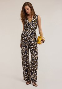 Kombinezon w kwiatowy wzór z peplum w talii, w odcieniach granatu, zieleni i kremu. Połączony z żółtą torebką i sandałami na obcasie.