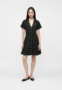 Čierne kárované šaty s krátkymi rukávmi, výstrihom do V, prednými gombíkmi, rozšírenou sukňou a textúrovanou látkou s bielou mriežkou.
