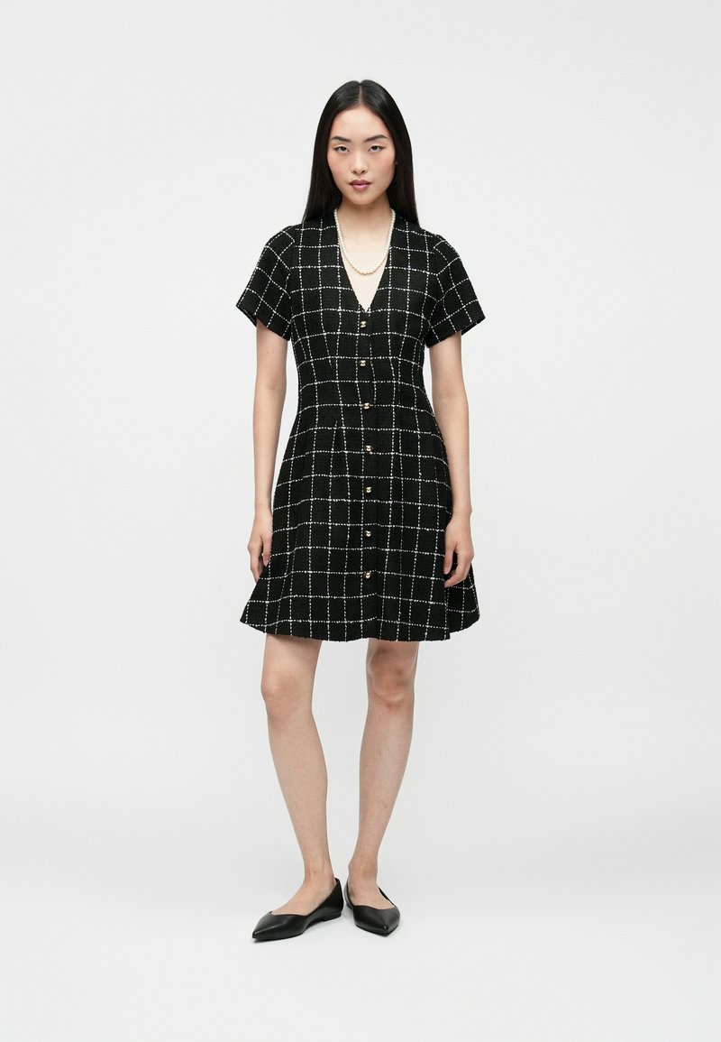 Čierne kárované šaty s krátkymi rukávmi, výstrihom do V, prednými gombíkmi, rozšírenou sukňou a textúrovanou látkou s bielou mriežkou.
