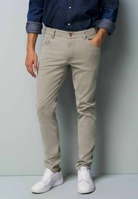 Beige Slim-Fit-Hosen mit glatter Textur, fünf Taschen und einem Knopfverschluss, kombiniert mit weißen Sneakers.