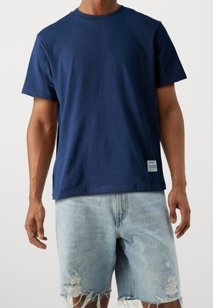 Marineblaues Baumwoll-T-Shirt mit kurzen Ärmeln und Rundhalsausschnitt, kombiniert mit hellblauen, verwaschenen Denim-Shorts mit ausgefransten Kanten.